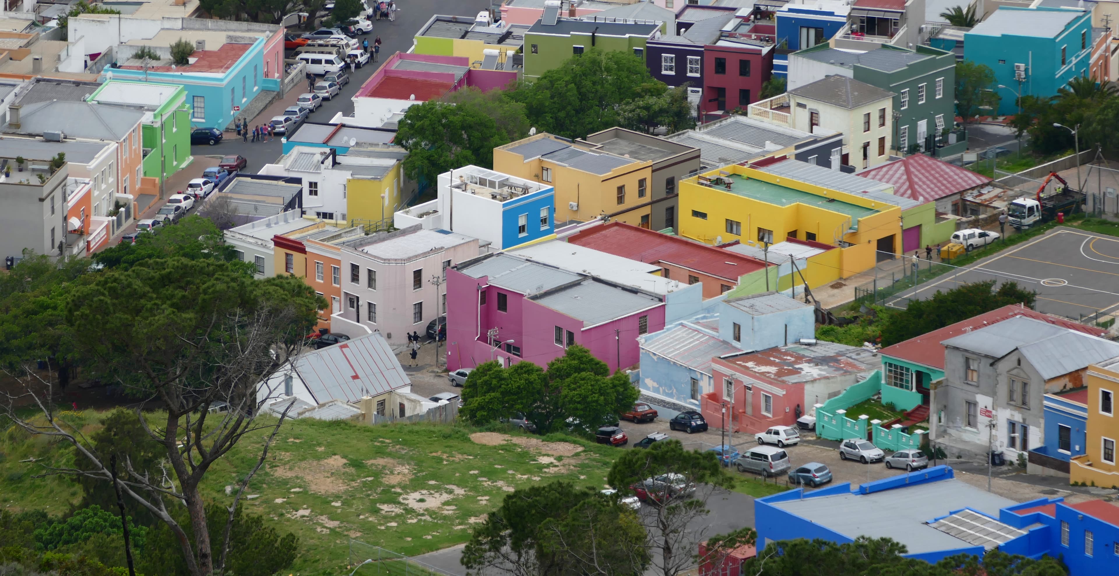 A row of brightly painted houses in vivid pink, blue, green, and yellow along a street in the Bo-Kaap district of Cape Town, South Africa, on the slopes of Signal Hill.