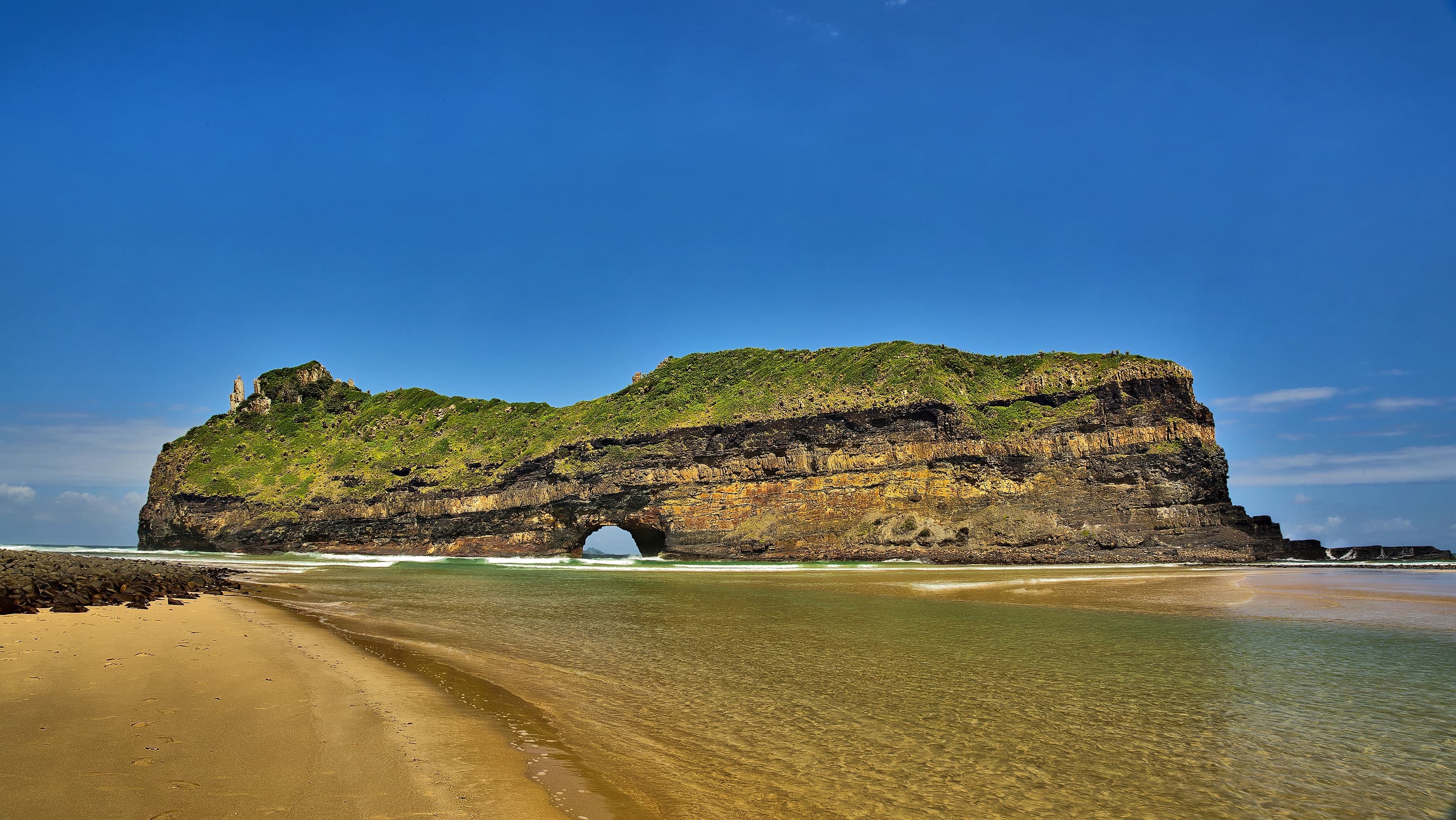 The Hole in the Wall sea arch, a large sandstone-and-shale rock island with a natural archway pierced through it by the sea, on the Wild Coast near Coffee Bay, Eastern Cape, South Africa.