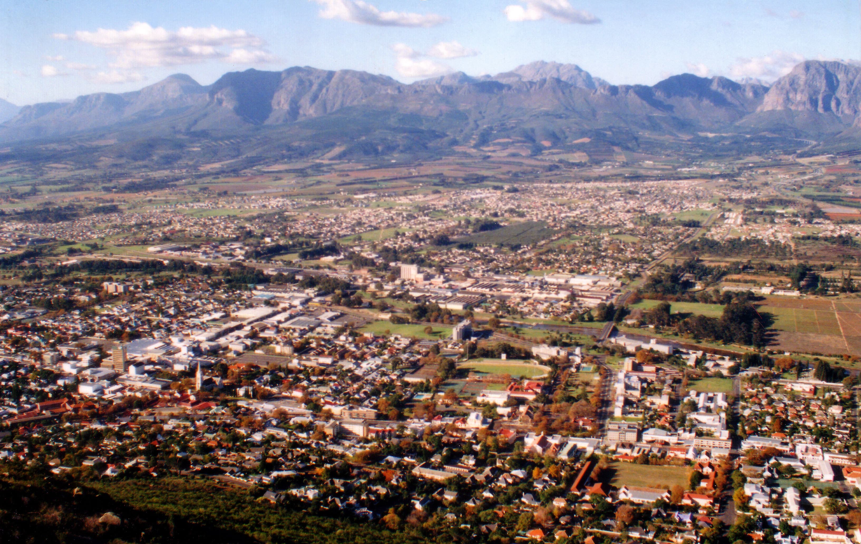 A landscape view of the town of Paarl in the Western Cape, South Africa, with buildings nestled among trees and mountains rising in the background.